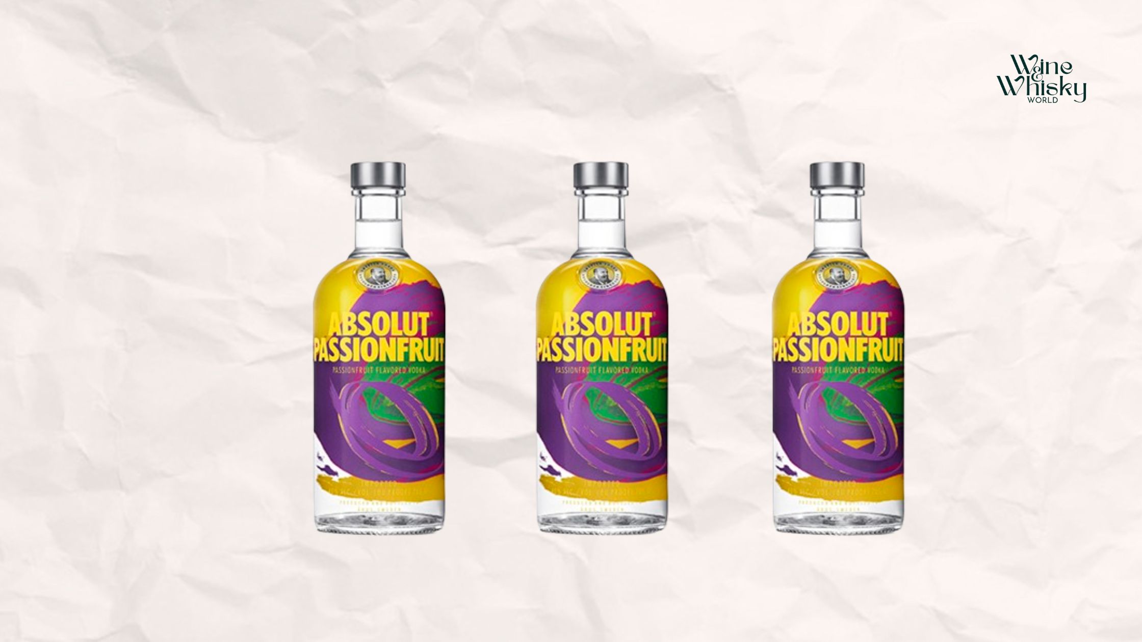 Clear glass bottle of Absolut Vodka passionfruit with brown and black text on the label, reading 'Absolut Vodka', displayed against a crumpled white paper background with the Wine Whisky World logo in the top right corner.